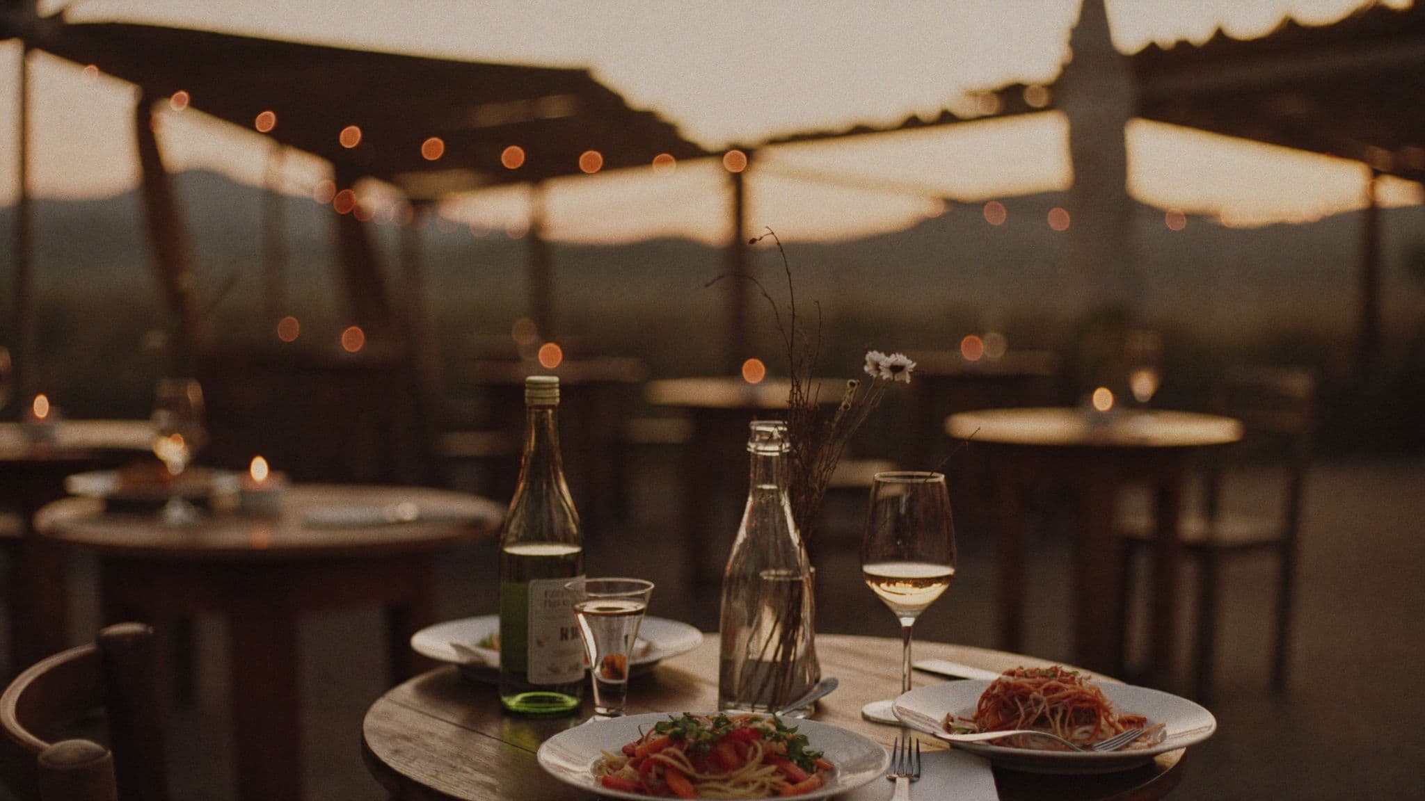 A taverna terrace at dusk, tables set under string lights
